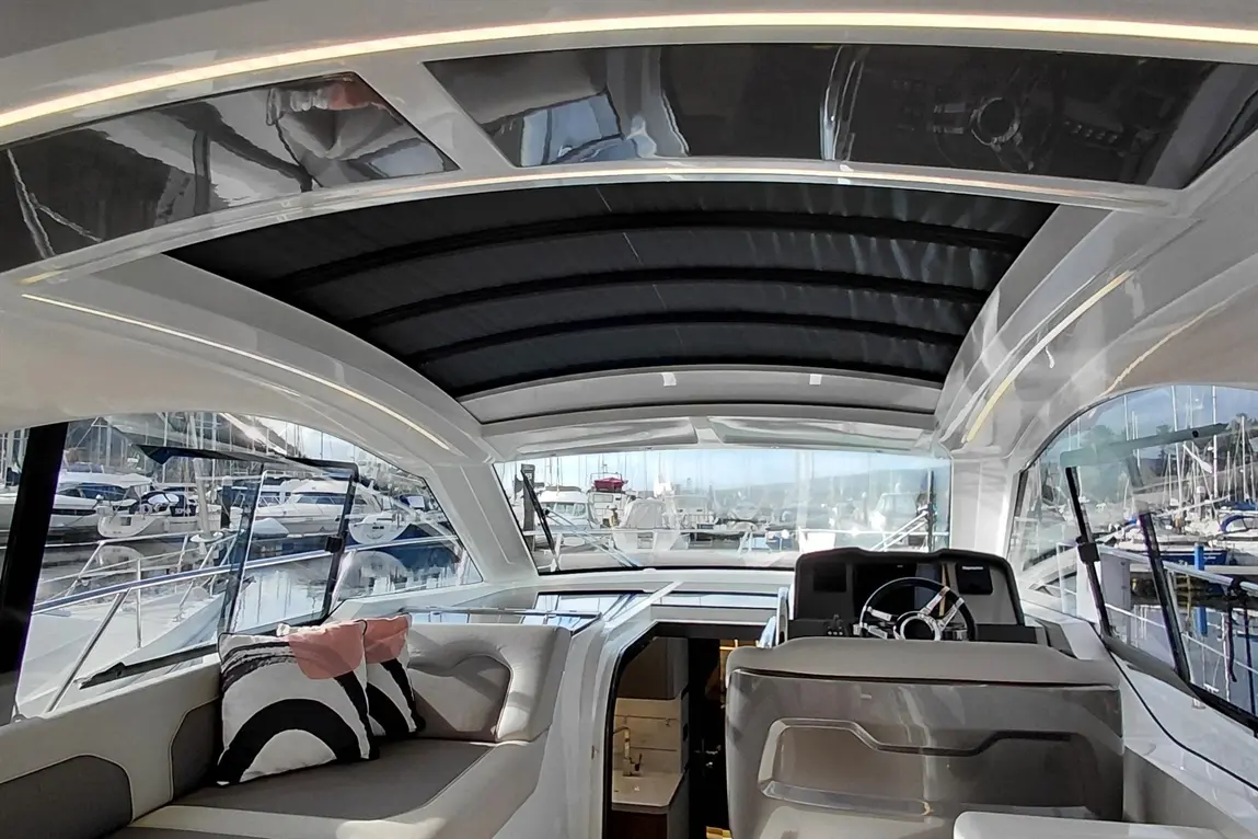 Interior of a modern yacht showcasing a sleek cabin, steering wheel, and plush seating with a view of a marina outside.